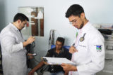 O aluno de medicina Carlos Eduardo Garcia, de 27 anos, é supervisionado pelo médico e instrutor, Estevão Cubas Rolim (de óculos) enquanto atende paciente na UBS 2 do Itapoã.