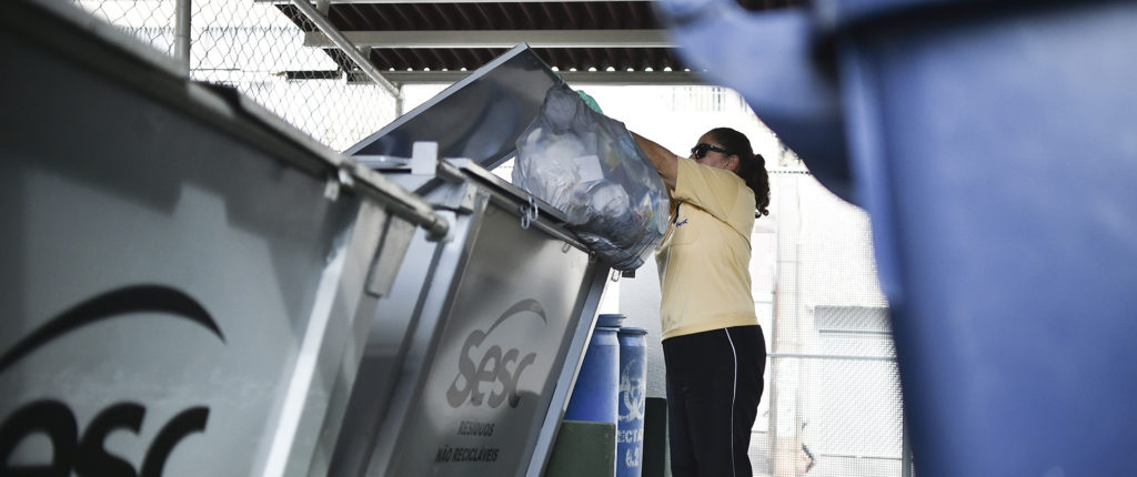 Mulher descarta saco lixo em caçamba de lixo